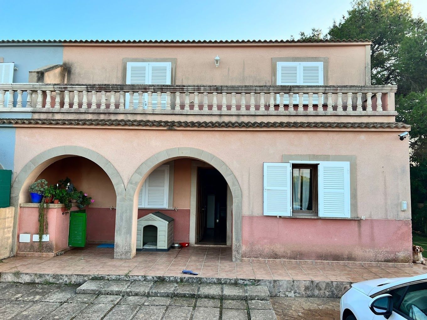 Una casa rosa con un coche aparcado delante.