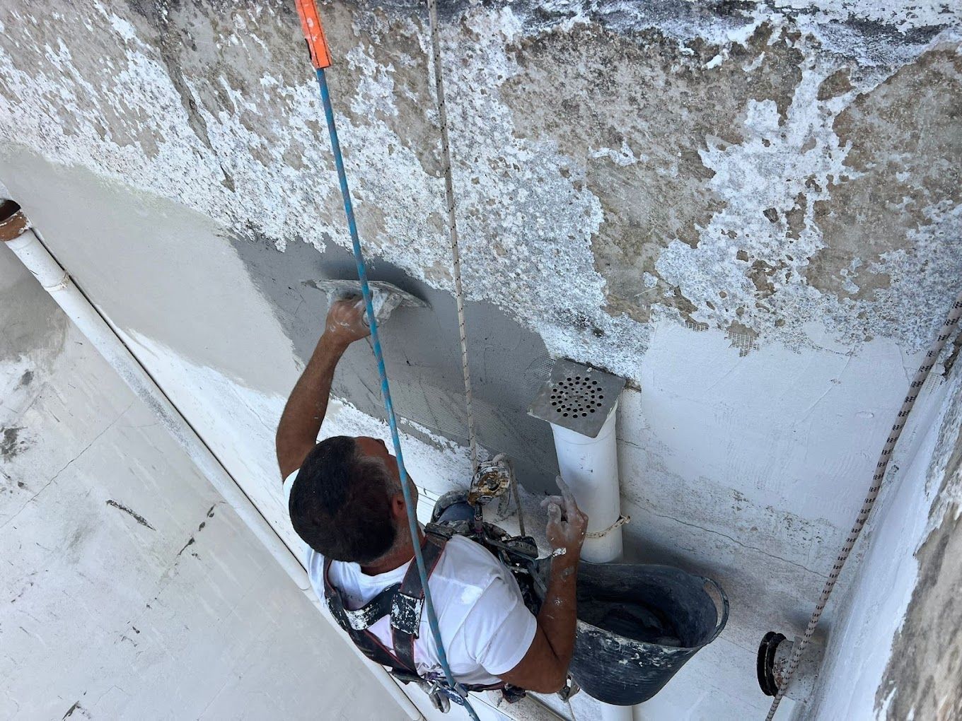 Un hombre está colgado de una cuerda y pintando una pared.