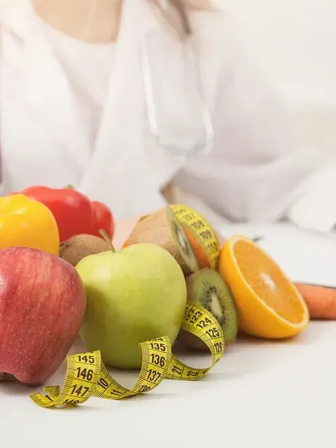 Un médico está sentado en una mesa con fruta y una cinta métrica.