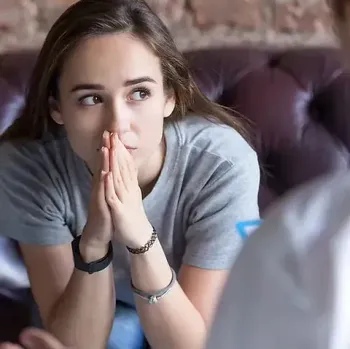 Una mujer está sentada en un sofá con las manos en la cara.
