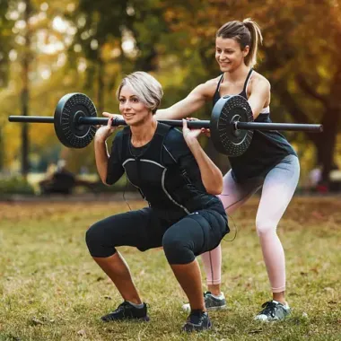 Dos mujeres están en cuclillas con pesas en un parque.