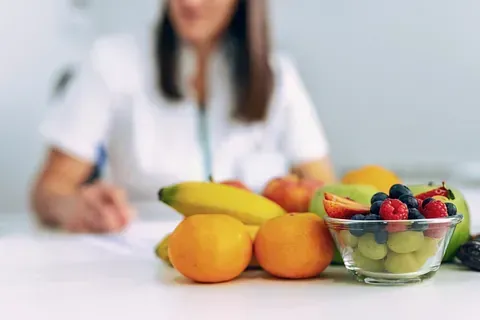 Una mujer está sentada en una mesa con un bol de fruta.