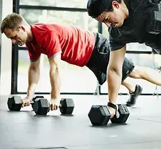 Dos hombres están haciendo flexiones con mancuernas en un gimnasio.