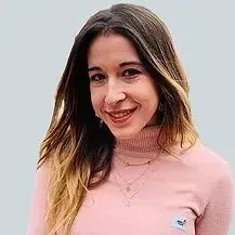 Una mujer lleva un suéter rosa y sonríe a la cámara.
