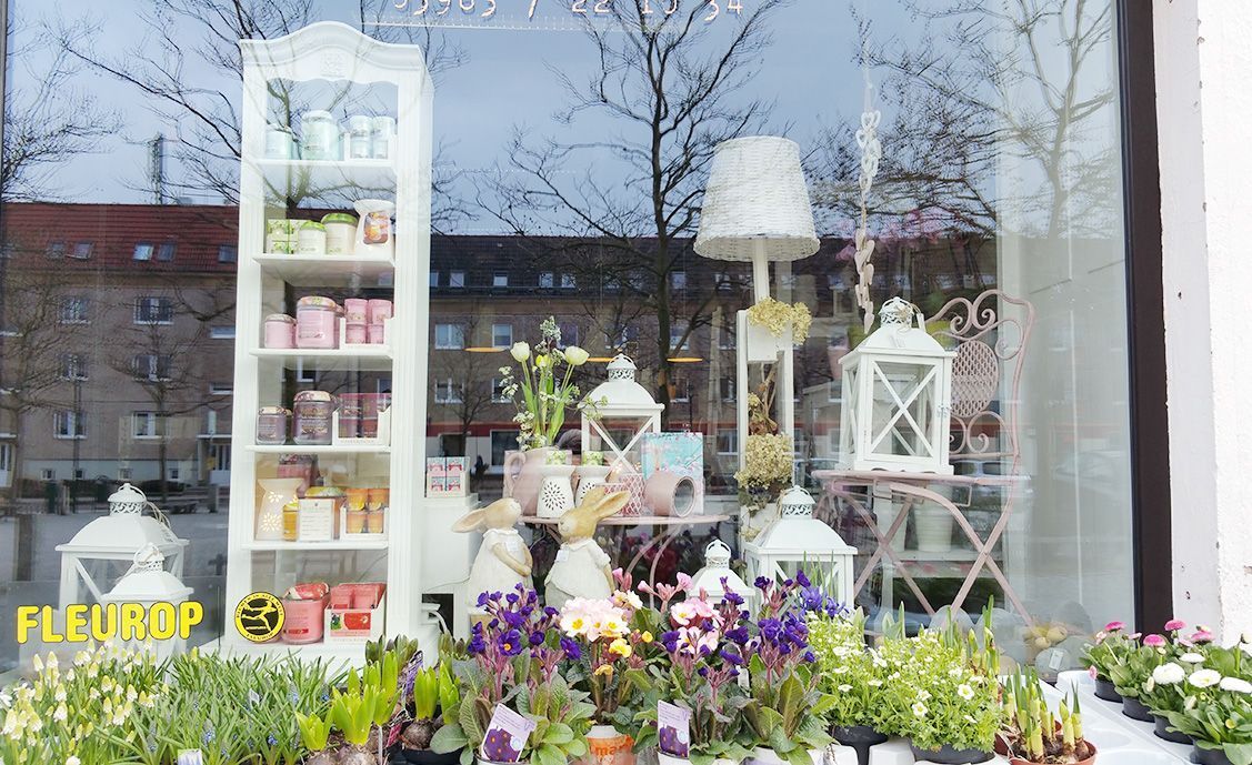 Blumen Liebe Woldegk - das Schaufenster des Blumenladens mit verschiedenen Gestecken, im Vordergrund ein Stand mit Blumen zum Verkauf