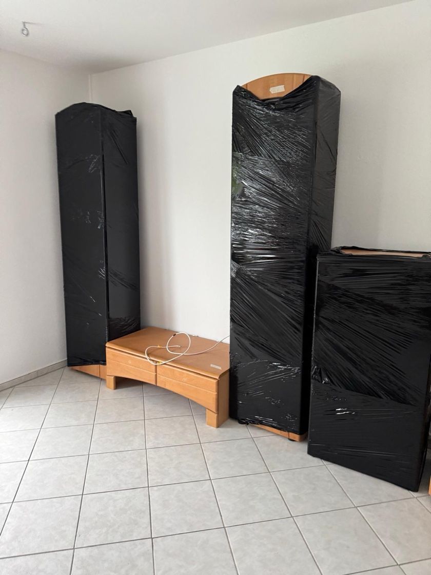 In schwarze Plastikfolie eingewickelte Möbel in einem Raum mit gefliestem Boden und weißen Wänden.