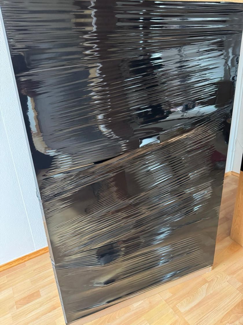 Schwarz verpackter Gegenstand, möglicherweise Möbel, auf einem Holzboden.