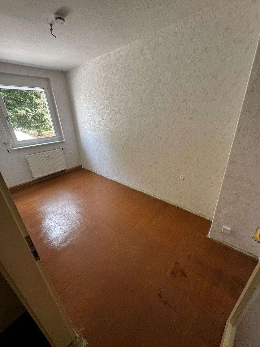 Leerer Raum mit dunklem Holzboden, strukturierten weißen Wänden und einem Fenster.