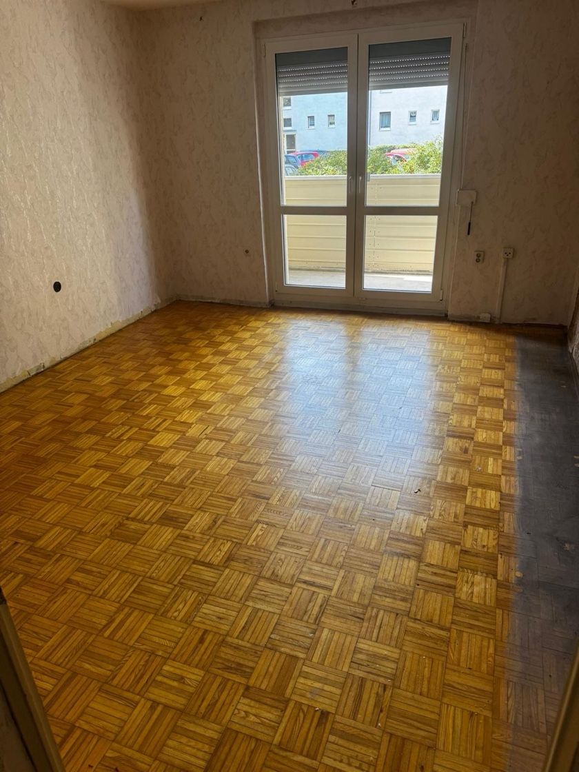 Leerer Raum mit Parkettboden, Fenster und hellen Wänden.