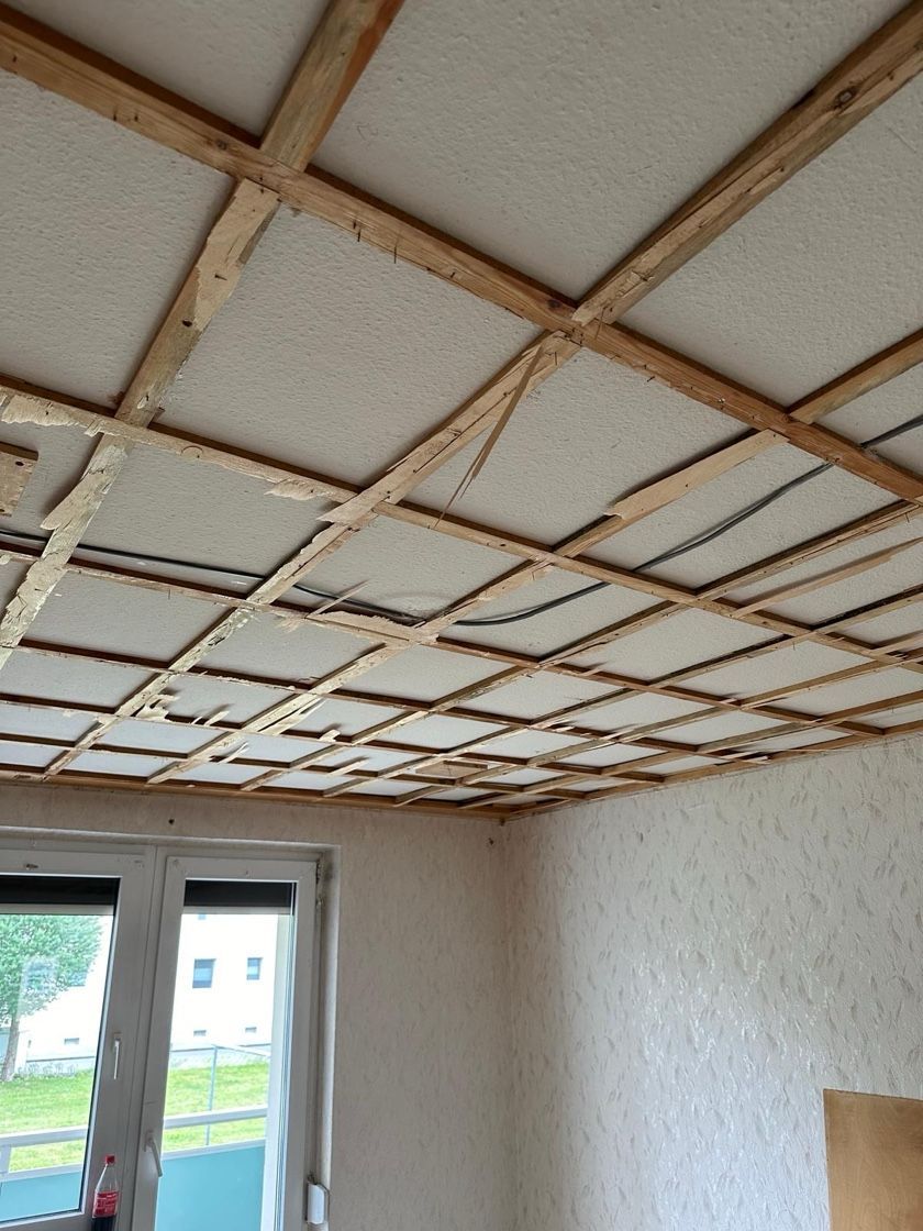 Innenansicht eines Raumes mit freiliegendem Holzdeckenrahmen und strukturierten Wänden. Fenster im Hintergrund.