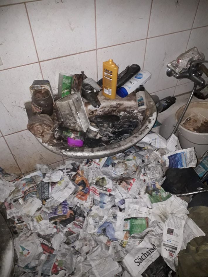 Eine unordentliche Ecke: Müll, Toilettenartikel und verbrannter Schutt auf einem kleinen Tisch neben einer gefliesten Wand.