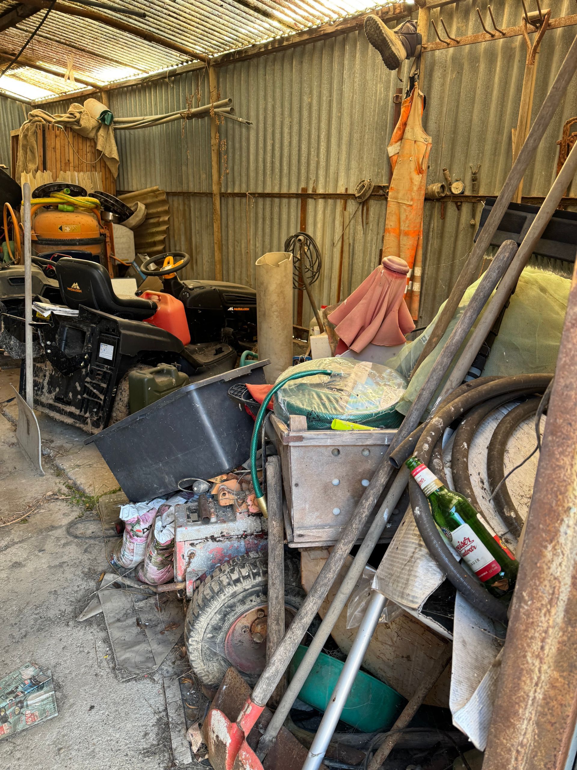 Überfülltes Schuppeninneres mit Werkzeugen, Maschinen und verschiedenen Gegenständen. Metallwände und Wellblechdach.