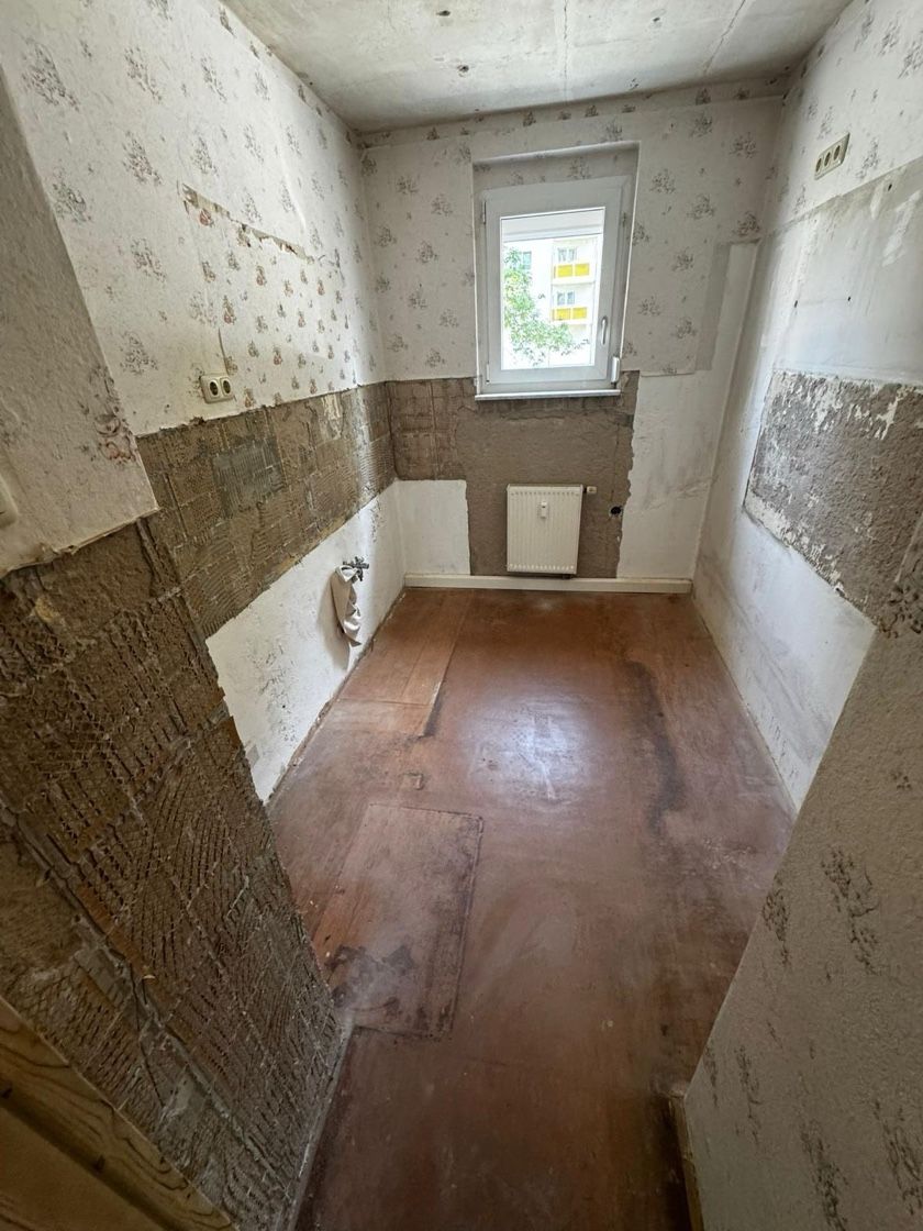 Badezimmereinrichtung mit abblätternder Tapete, freiliegender Wand und braunem Boden.