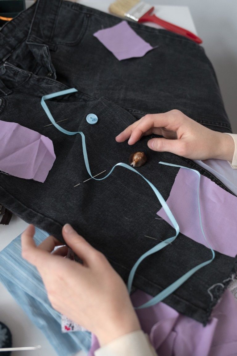 Manos trabajando en una manualidad sobre tela negra con costuras azul claro y patrones de papel morado.
