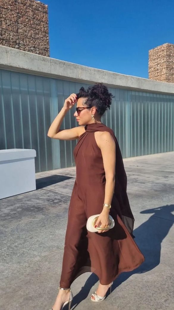 Una persona con un vestido marrón sin mangas camina al aire libre .