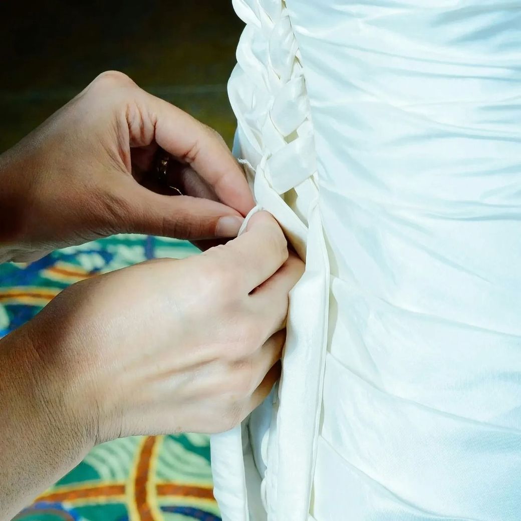 Unas manos atan la parte trasera de un vestido blanco con cintas.