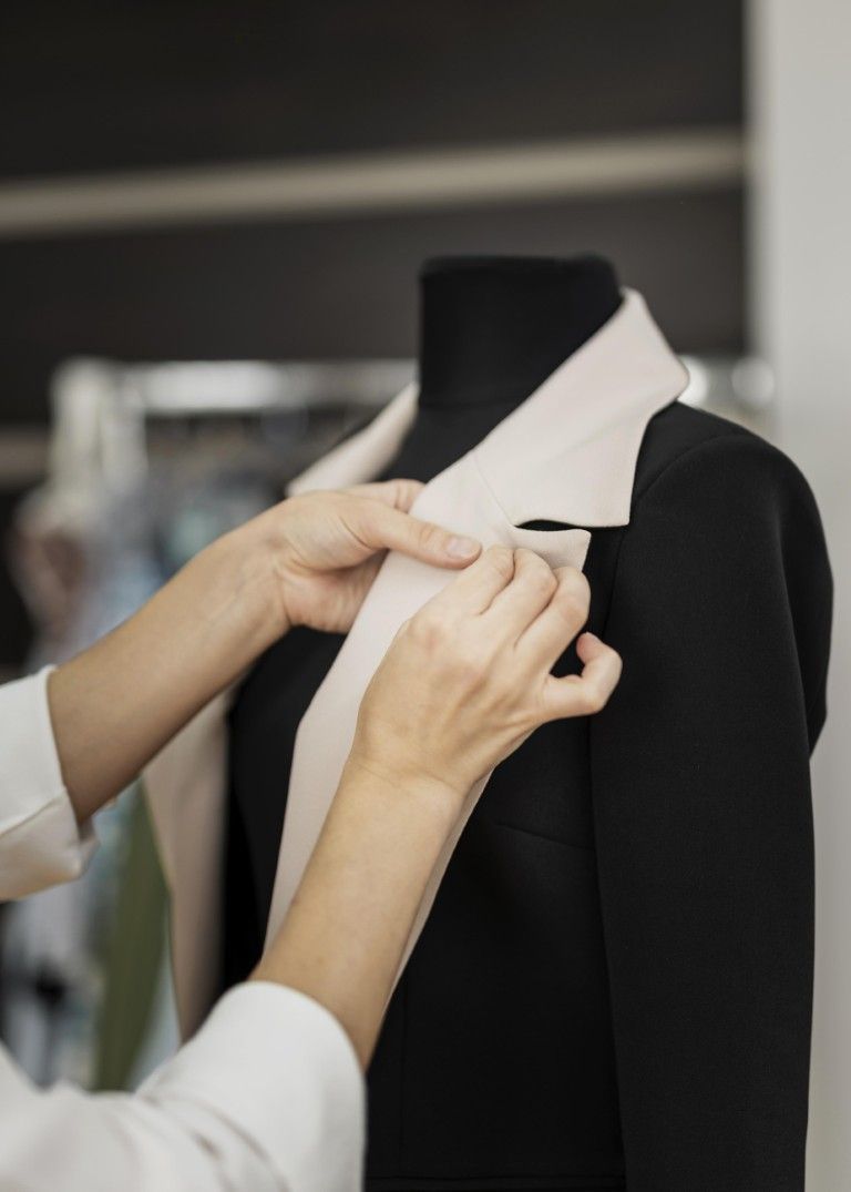 Manos ajustando un cuello blanco en un maniquí negro en un taller de sastrería.