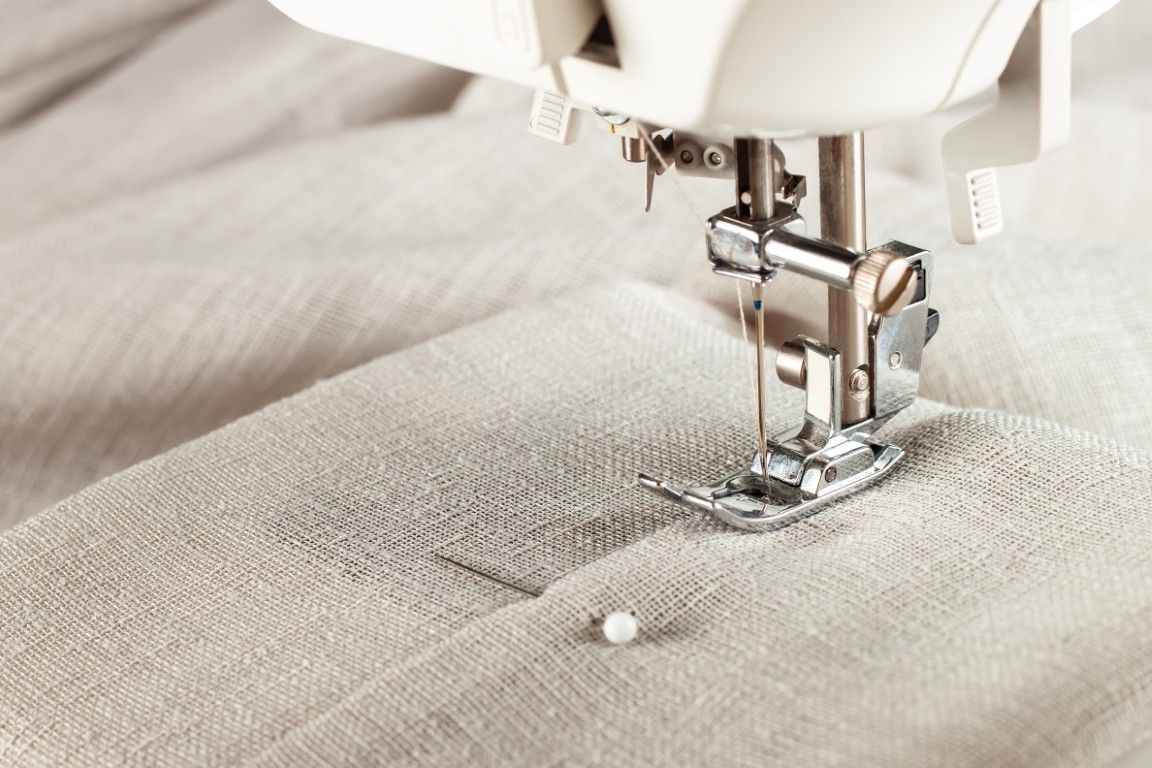 Primer plano de una aguja de máquina de coser cosiendo tela beige