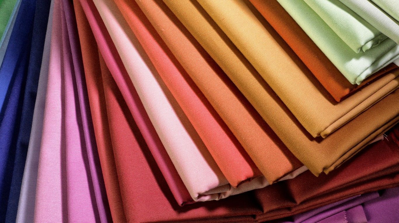 Telas o retazos de tela coloridos, doblados y apilados, en tonos rosa, morado, naranja y verde.
