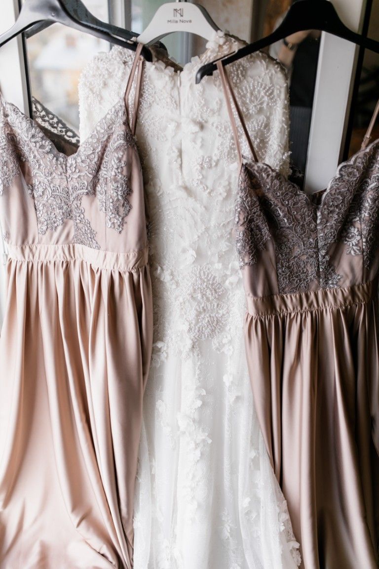Dos vestidos color rosa empolvado y encaje colgados en perchas, con faldas de satén y corpiños bordados.
