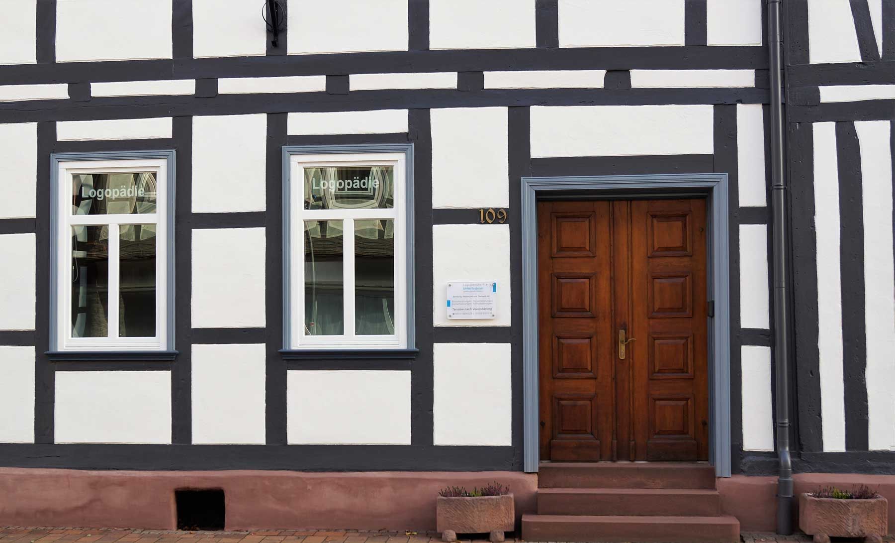 Fachwerkfassade mit weißen und dunkelgrauen Paneelen, zwei Fenstern und einer Holztür.