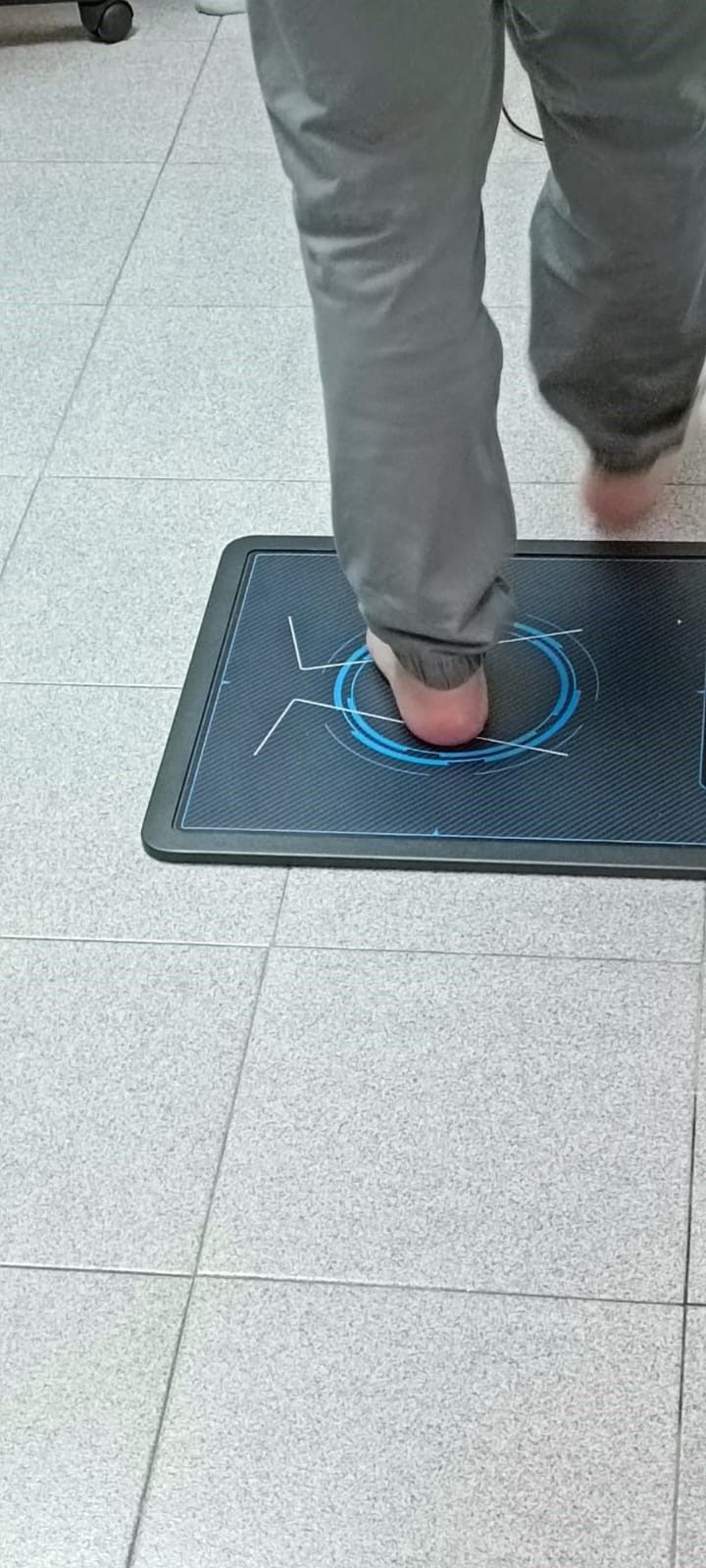 Persona pisando una alfombrilla sensora negra con anillos azules sobre un suelo de baldosas