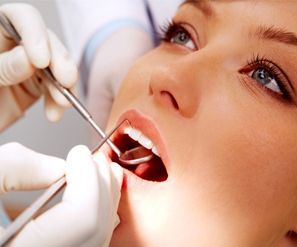 Dentista utilizando instrumentos para examinar la boca abierta de un paciente durante una revisión dental