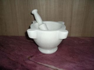 Mortero y maja de mármol blanco sobre una encimera de color morado.