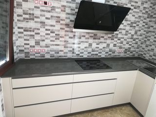 Cocina moderna con encimeras grises, gabinetes beige y salpicadero de azulejos.