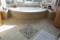 Baño con bañera de hidromasaje redonda, suelo de baldosas beige y un azulejo decorativo en el centro.