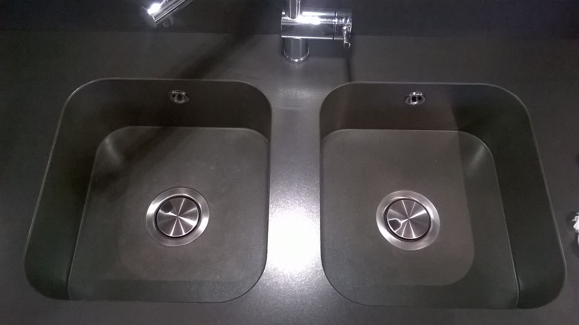Dos fregaderos de cocina de acero inoxidable con grifo, colocados en una encimera oscura.