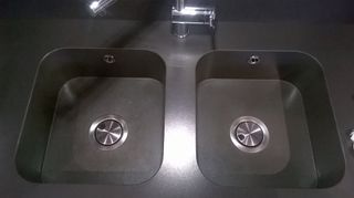 Dos fregaderos de cocina de acero inoxidable con grifo, colocados en una encimera oscura.