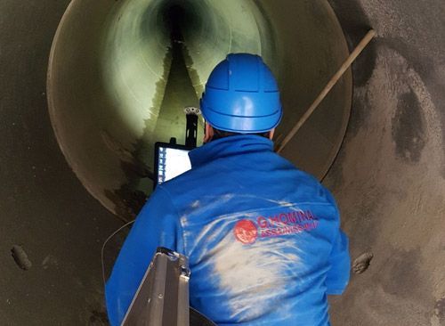 Un homme portant une veste bleue se tient dans un tunnel et regarde un écran d'ordinateur.