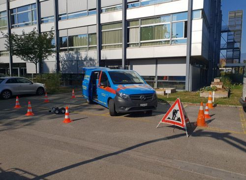 Une camionnette bleue est garée sur un parking à côté d'un bâtiment.