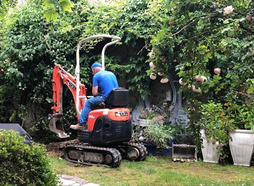 Un homme est assis sur une petite excavatrice dans un jardin.