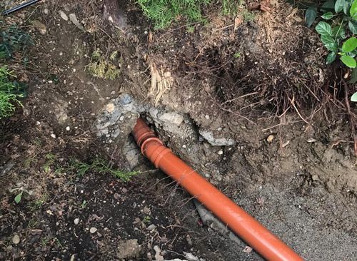 Un tuyau rouge repose dans la terre à côté d'un rocher.