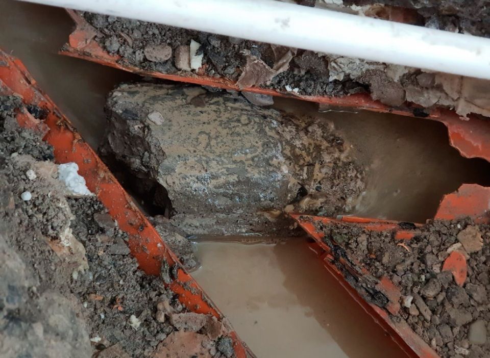 Un gros rocher repose dans la terre à côté d'un tuyau.