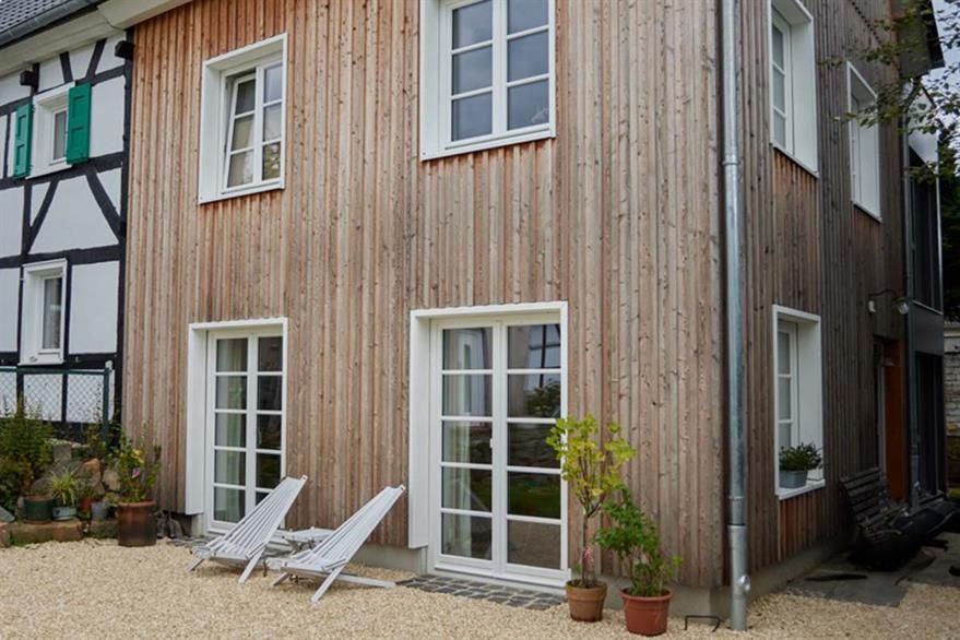 Ein Holzhaus mit vielen Fenstern und Stühlen davor.