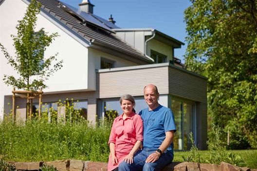 Ein Mann und eine Frau sitzen auf einem Felsen vor einem Haus.
