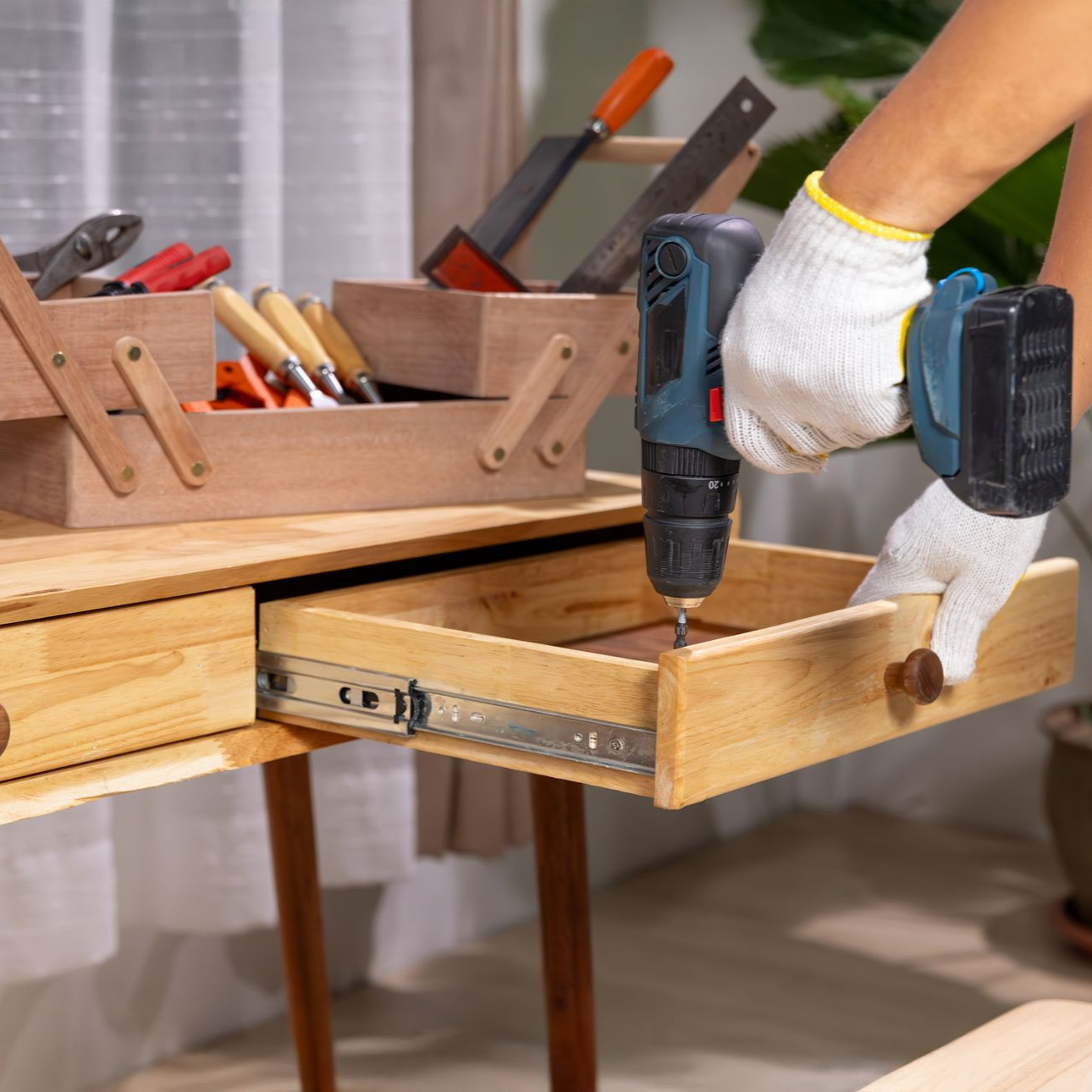 Un homme utilisant une perceuse électrique pour installer un tiroir dans un bureau en bois.