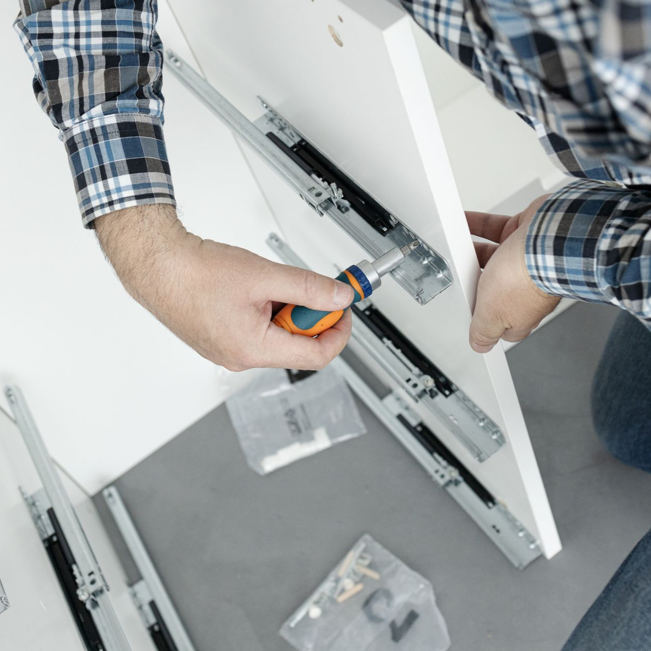 Personne assemblant des meubles, utilisant un tournevis pour fixer des glissières de tiroir à une armoire blanche.