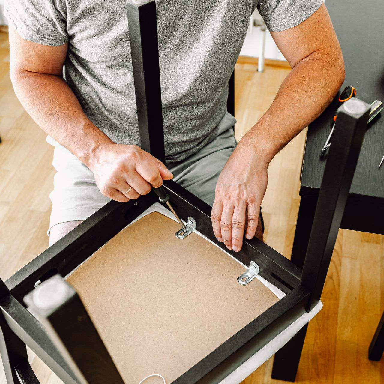 Une personne assemble une chaise noire, en travaillant à la main sur la face inférieure.