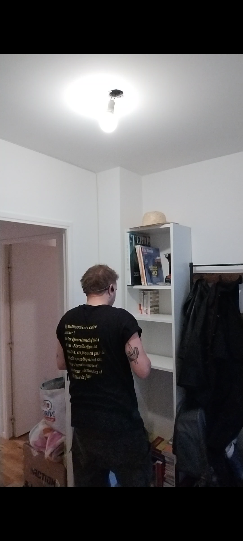 Un homme en combinaison bleue assemble une étagère blanche en consultant la notice.