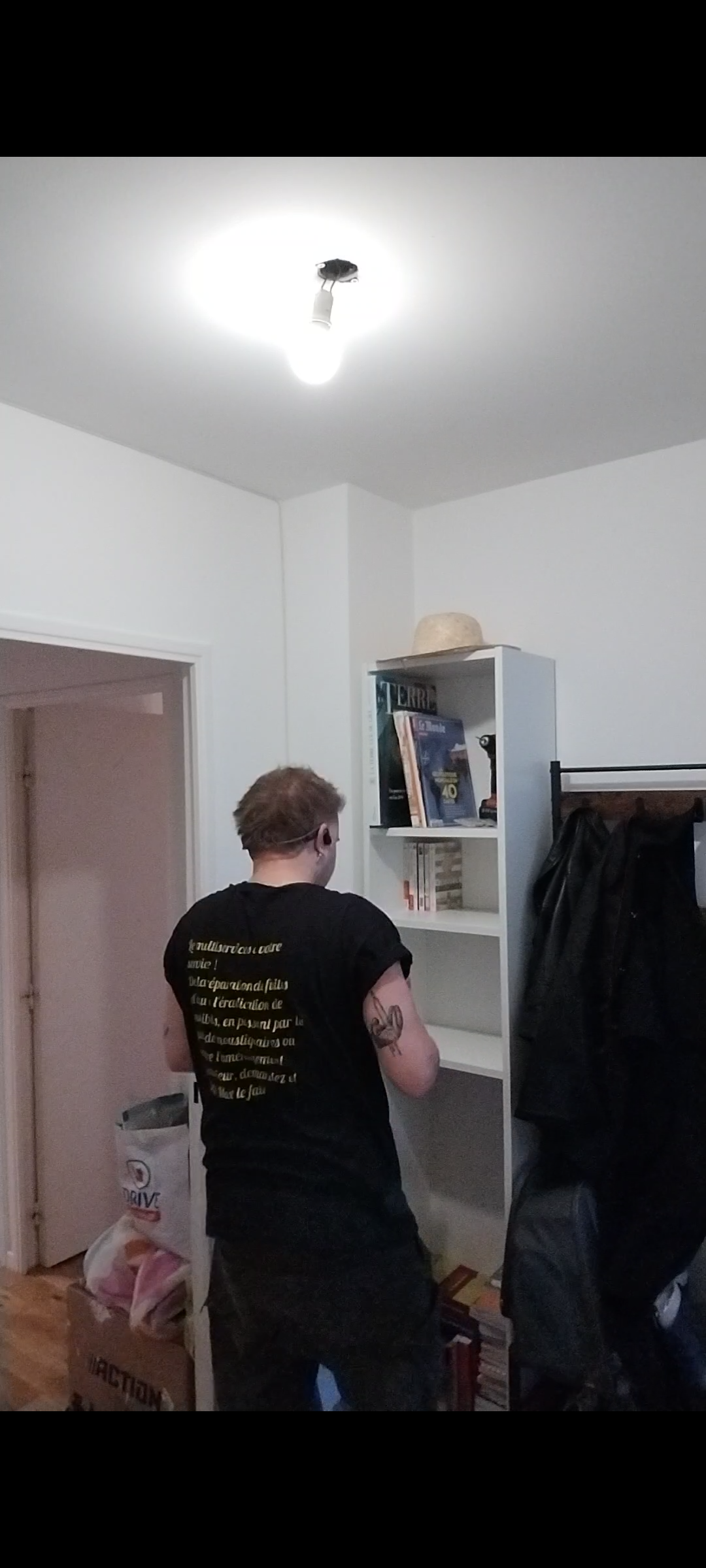 Un homme en combinaison bleue assemble une étagère blanche en consultant la notice. 