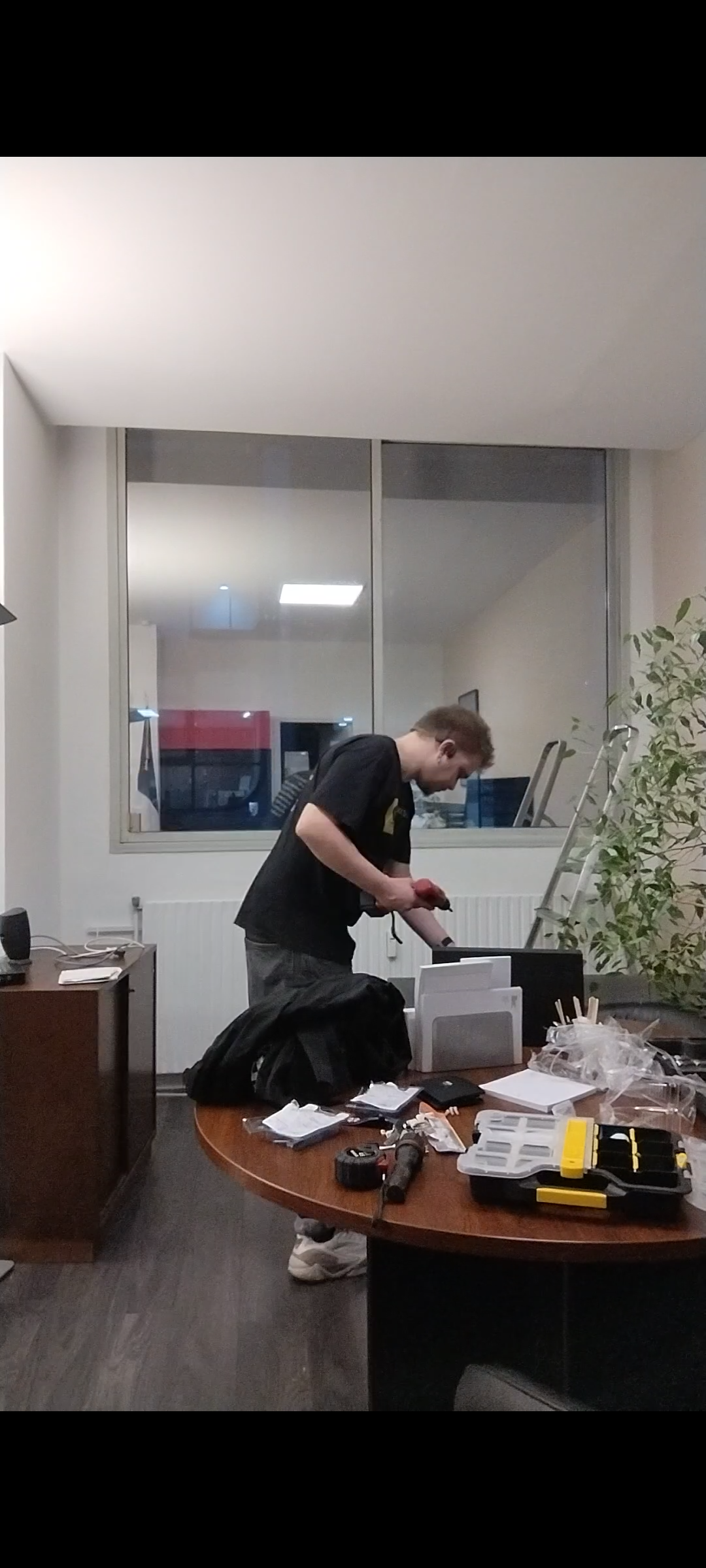 Personne en jeans bleu foncé et gants jaunes portant une boîte à outils rouge et grise.