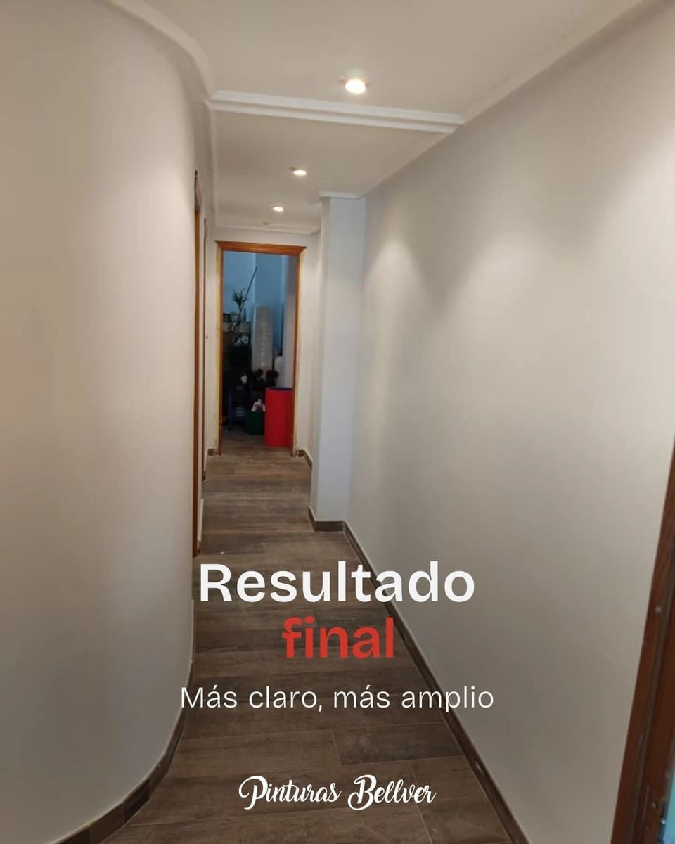 Pasillo estrecho con paredes blancas y luces empotradas, que deja ver un espacio terminado más amplio al final.