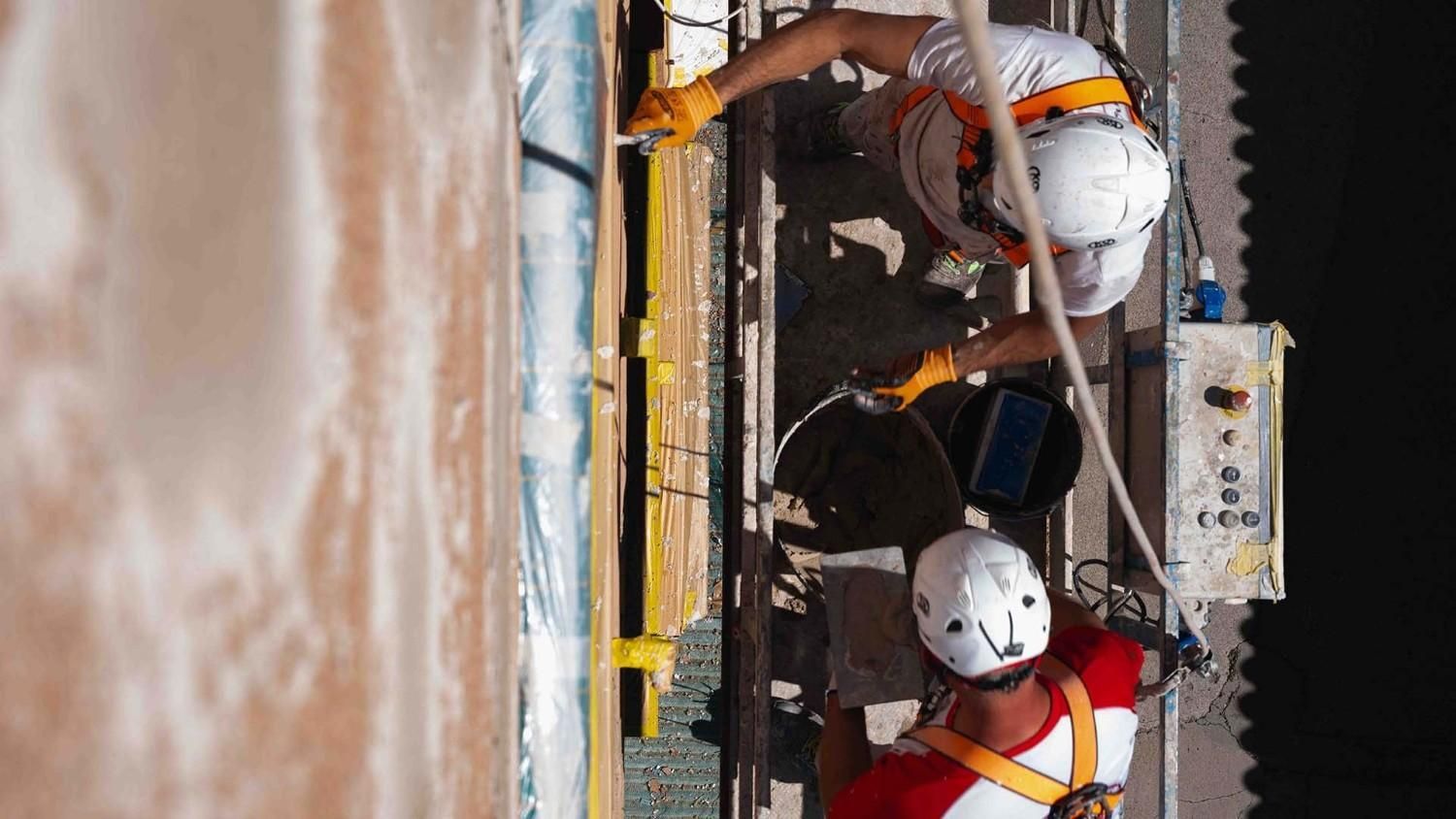 Dos trabajadores, con arneses de seguridad y cascos blancos