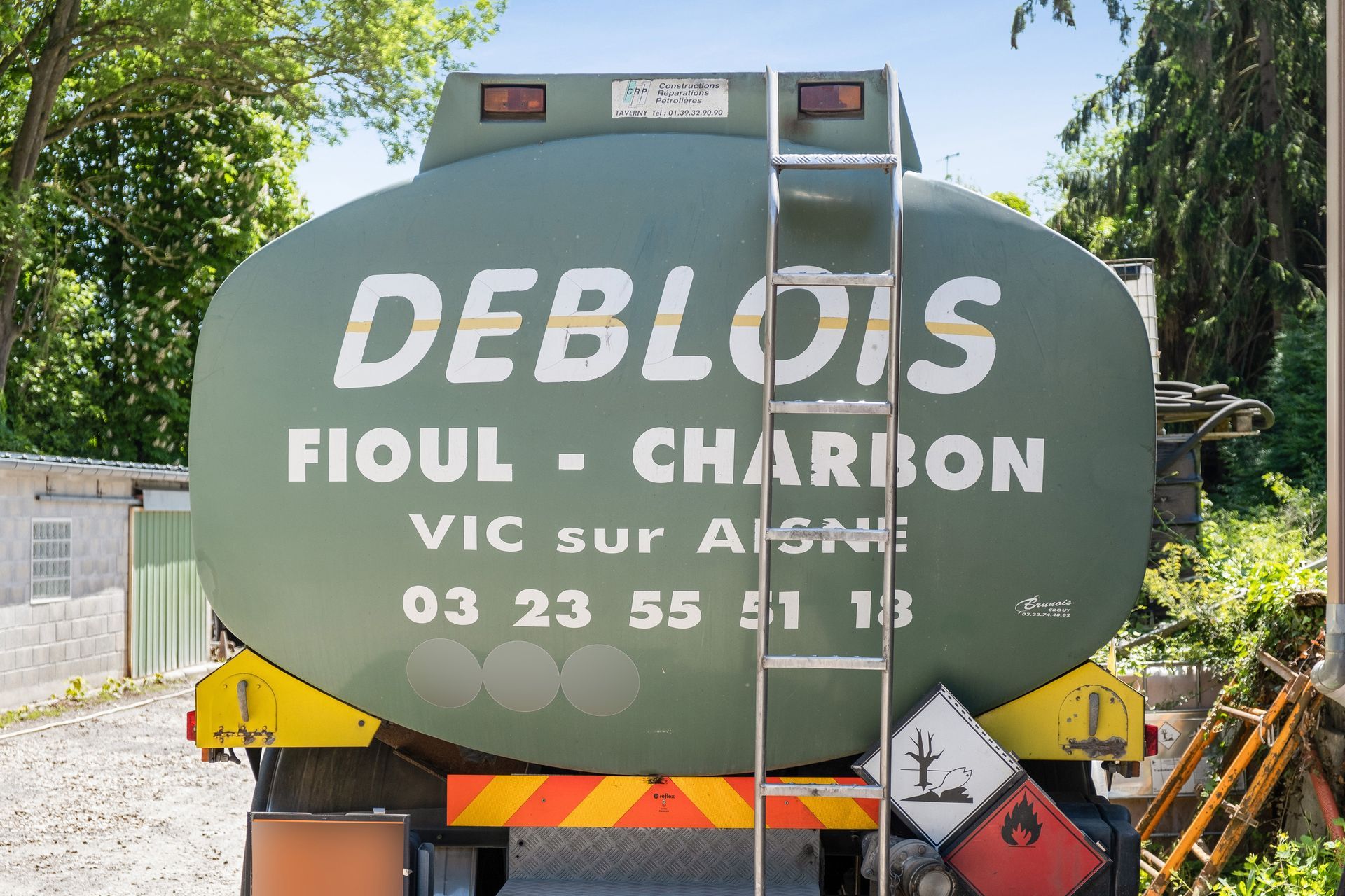 Un camion-citerne vert stationné à l'extérieur avec l'inscription « DEBLOIS FIOUL - CHARBON » et un numéro de téléphone imprimés à l'arrière de sa cuve.