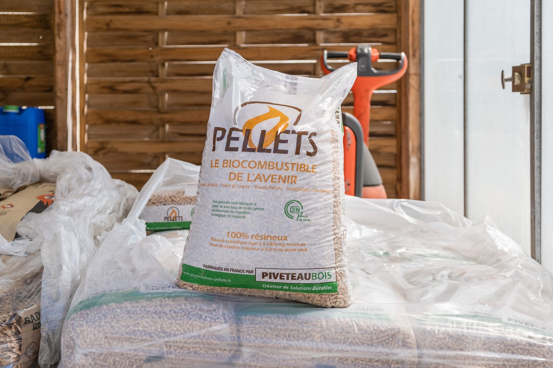 Un sac de granulés de bois posé sur une palette dans un hangar, avec un transpalette en arrière-plan.