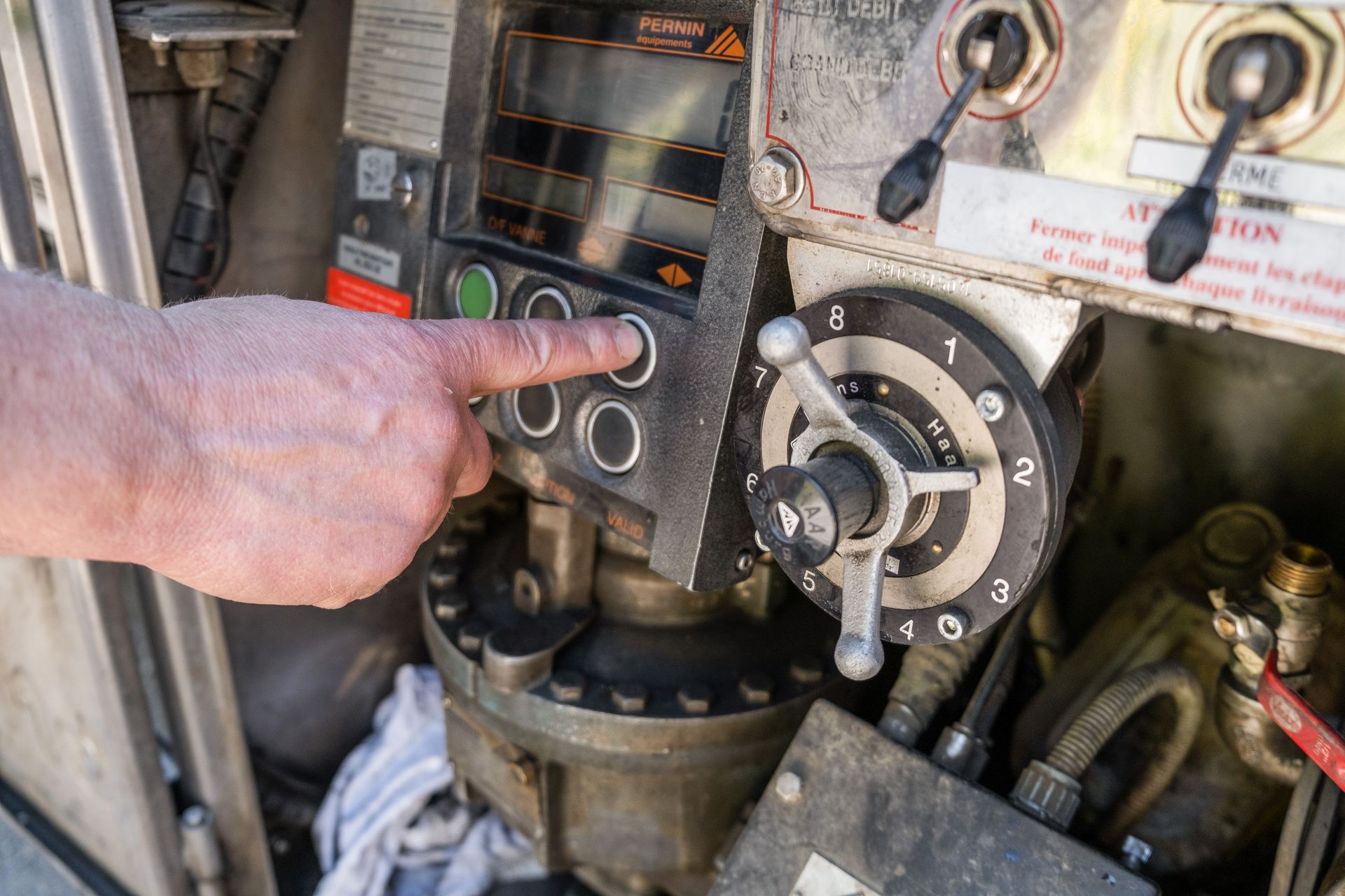 Une main appuie sur un bouton circulaire d'un panneau de commande industriel, à côté d'un cadran rotatif numéroté.